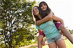 Girl giving her best friend a piggy back in park