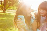 Two girls looking at smartphone in sunlit park