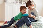 Male toddler and brother on beanbag chair looking at digital tablet