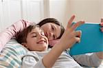 Boy and sister reclining on beanbag chair looking at digital tablet