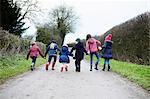 Rear view of boy and girls holding hands and fooling around on rural road