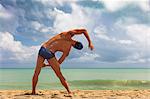 Rear view of muscular male swimmer on beach bending over sideways