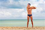 Muscular male swimmer standing on beach warming up