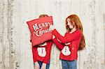 Portrait of twin sisters wearing Christmas jumpers, one sister covering sister's face with cushion
