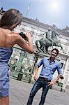 Young woman taking photograph of young man, using smartphone, Turin, Piedmont, Italy