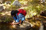 Young woman, hiking, crouching on rock beside stream, Cape Town, South Africa