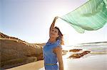 Mature woman standing on beach, holding sheer scarf in air, Cape Town, South Africa