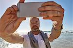 Mature man on beach, taking selfie with smartphone, Cape Town, South Africa