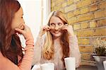 Two female friends, sitting outdoors, having coffee, fooling around