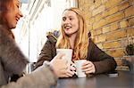 Two female friends, sitting outdoors, drinking coffee, laughing