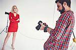 Male photographer reviewing shoot of female model on studio white background