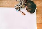 Overhead view of boy drawing on large paper on floor