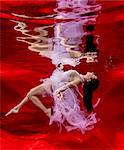 Underwater view of poised woman with flowing pink dress against red background