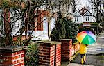 Rear view of boy in yellow anorak carrying umbrella along street