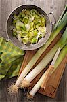 Whole leeks on a chopping board and sliced leeks in a colander