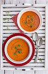 Two bowls of cream of tomato soup with fresh basil on a wooden tray