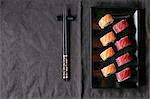 Sushi with salmon and tuna fish on a black plate next to chopsticks (Japan)