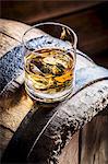 A glass of whiskey with ice on an old wooden barrel