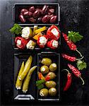 Various olives, stuffed mini peppers and jalapeños on a black baking tray