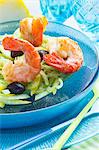 King prawns on a lemon and fennel salad with black olives on a glass turquoise plate