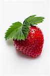 A strawberry with a leaf on a white surface