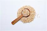 A pile of amaranth flakes with a wooden spoon on a white surface