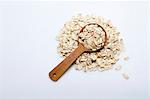 A pile of oats with a wooden spoon on a white surface