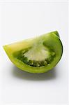 A wedge of green tomato on a white surface