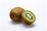 A whole kiwi and a halved kiwi on a white surface