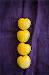 Four yellow tomatoes on a violet cloth