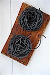 Two pasta nests made of black sepia pasta on a wooden board