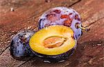 Whole and halved plums on a wooden surface