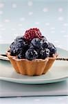 A blueberry tartlet with one raspberry
