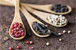 Four different types of pepper on wooden spoons