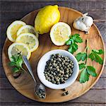 Lemons, capers, garlic and parsley on a wooden plate