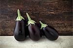Three aubergines in front of a wooden wall