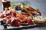 A starter platter with ham, breadsticks, olives and a dip