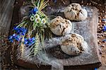 Healthy wholemeal bread rolls with ears of corn and field flowers on a wooden board