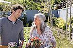 Happy couple carrying potted flowers, gardening in sunny garden