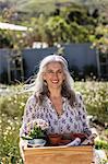 Portrait smiling mature woman carrying gardening tray in sunny garden