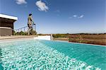 Businessman standing on luxury sunny patio with infinity pool, looking at view