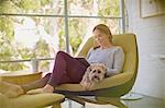 Woman with dog relaxing, using digital tablet in chair