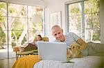 Smiling man with dog using laptop on bed