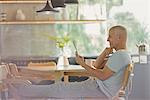 Mature man relaxing, using digital tablet with feet up at dining table