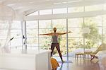 Woman practicing yoga with arms outstretched in sunny modern bedroom