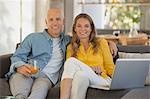 Portrait smiling mature couple using laptop on sofa