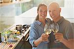 Portrait happy mature couple toasting white wine glasses, cooking in kitchen