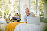 Mature couple relaxing, using laptop and digital tablet in bedroom