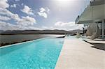 Sunny tranquil modern luxury home showcase exterior patio with infinity pool and ocean view