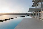 Sunny, tranquil modern luxury home showcase exterior with infinity pool and sunset ocean view